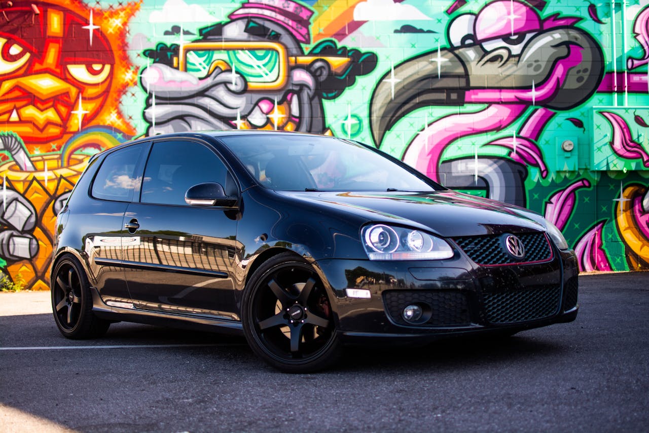 A black volkswagen golf gti parked in front of a graffiti wall
